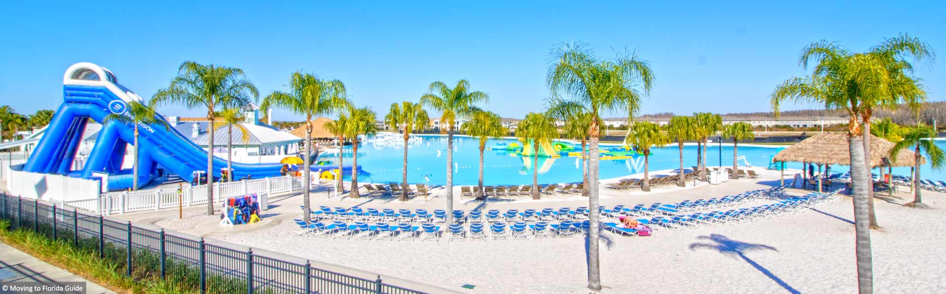 large swimming pool with water slide, chairs and palm trees