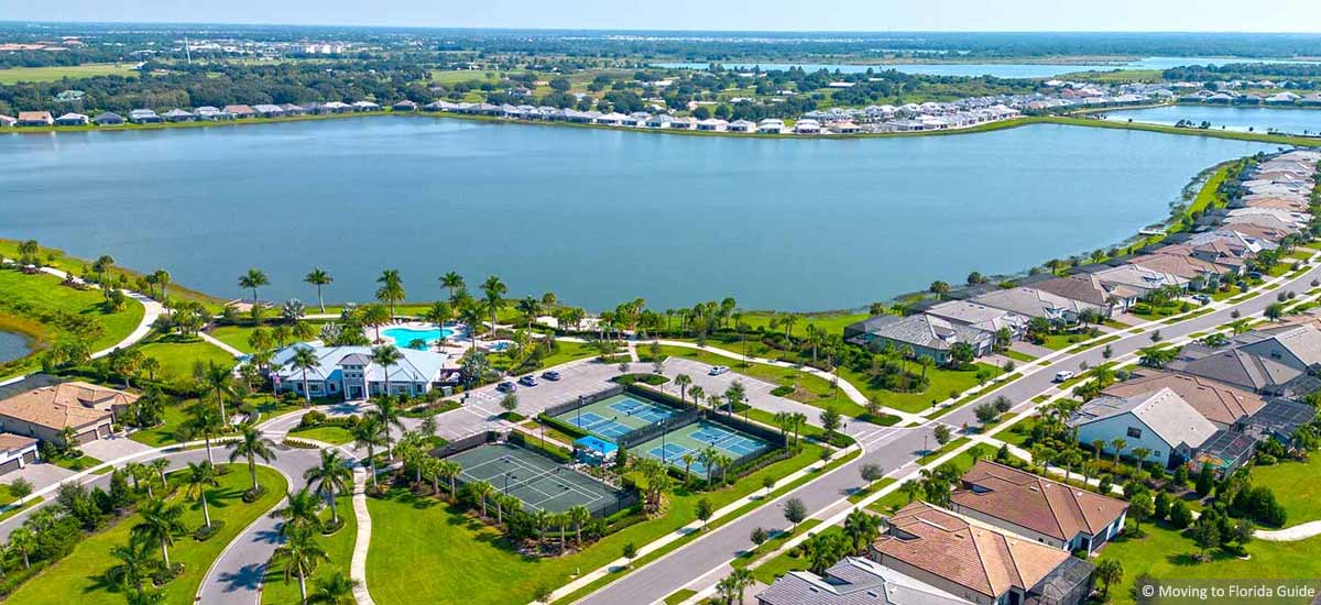 Florida homes around large lake with clubouse and tennis courts on sunny day